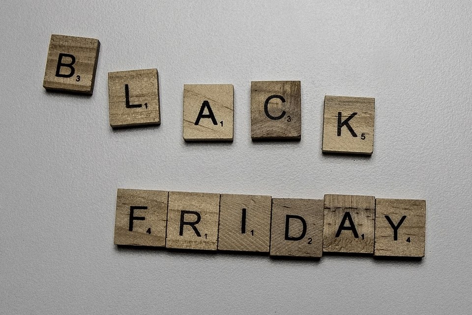 Black friday sale promotional text on wooden scrabble tiles with "black friday" spelled out on a neutral background, emphasizing shopping discounts, holiday sales, and e-commerce deals.