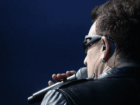 A musician performing live on stage with a microphone, wearing sunglasses and headphones, captured in a dynamic concert setting.