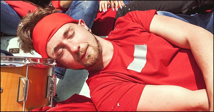 Energetic young man sleeping peacefully after music festival, surrounded by drums, showcasing music event culture and festival lifestyle.