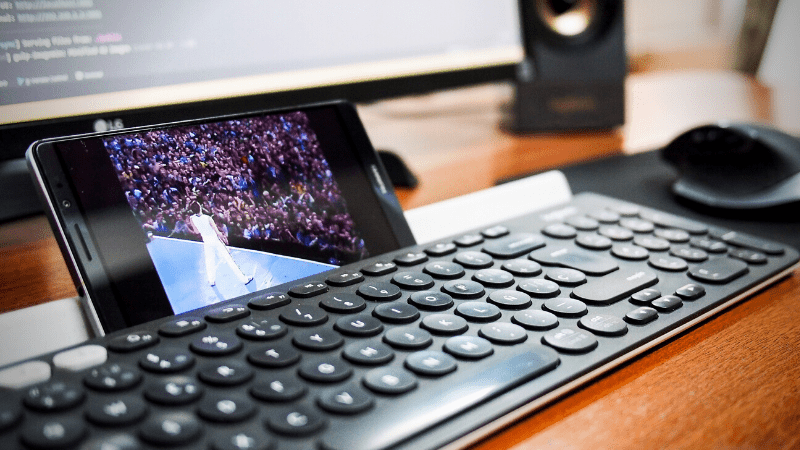 Keyboard with smartphone displaying a concert performance on screen, computer monitor in background - music industry tech, live event streaming, digital music production, artist promotions, music marketing tools, Hypebot.