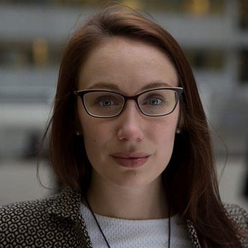 Modern woman wearing glasses, outdoor urban setting, professional headshot, business attire, red hair, potential interview or corporate profile image.