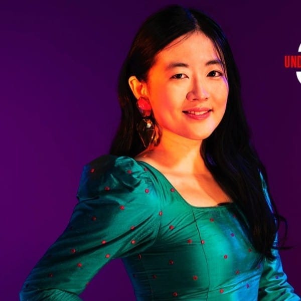 Hypebot article featuring Asian woman presenter at music industry event, vibrant background, professional speaker, entertainment industry insights, live event coverage, digital media, music marketing strategies.