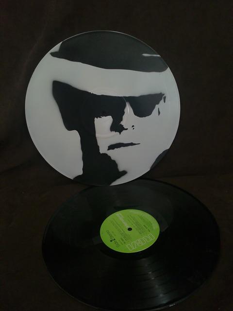 Vinyl record with an image of a person's face wearing sunglasses and a hat, displayed alongside a green-labeled turntable.
