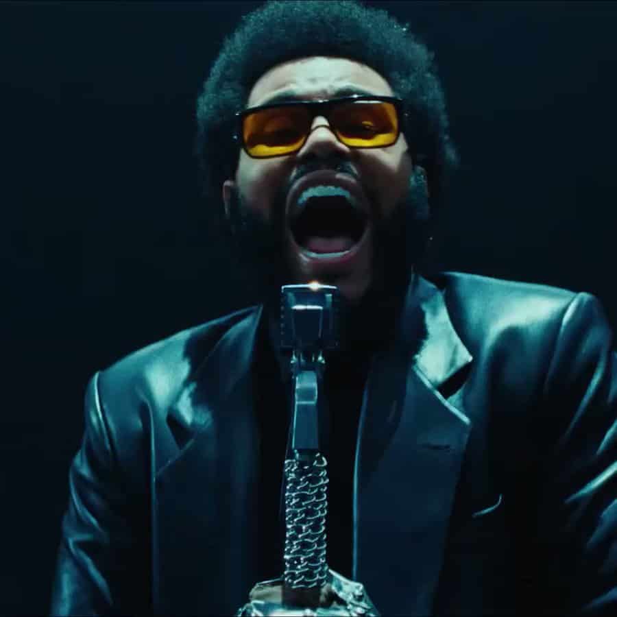 Viral singer performing passionately with microphone, wearing sunglasses and retro style leather jacket, in a dynamic stage setting for music and entertainment news.