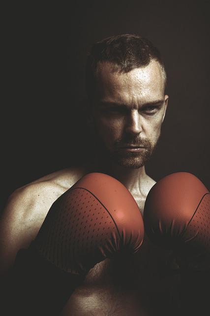 Boxing fighter with red gloves and intense expression in dark background, sports and fitness concept, male athlete ready for boxing match, concentration and determination in his eyes, professional training, combat sports image.
