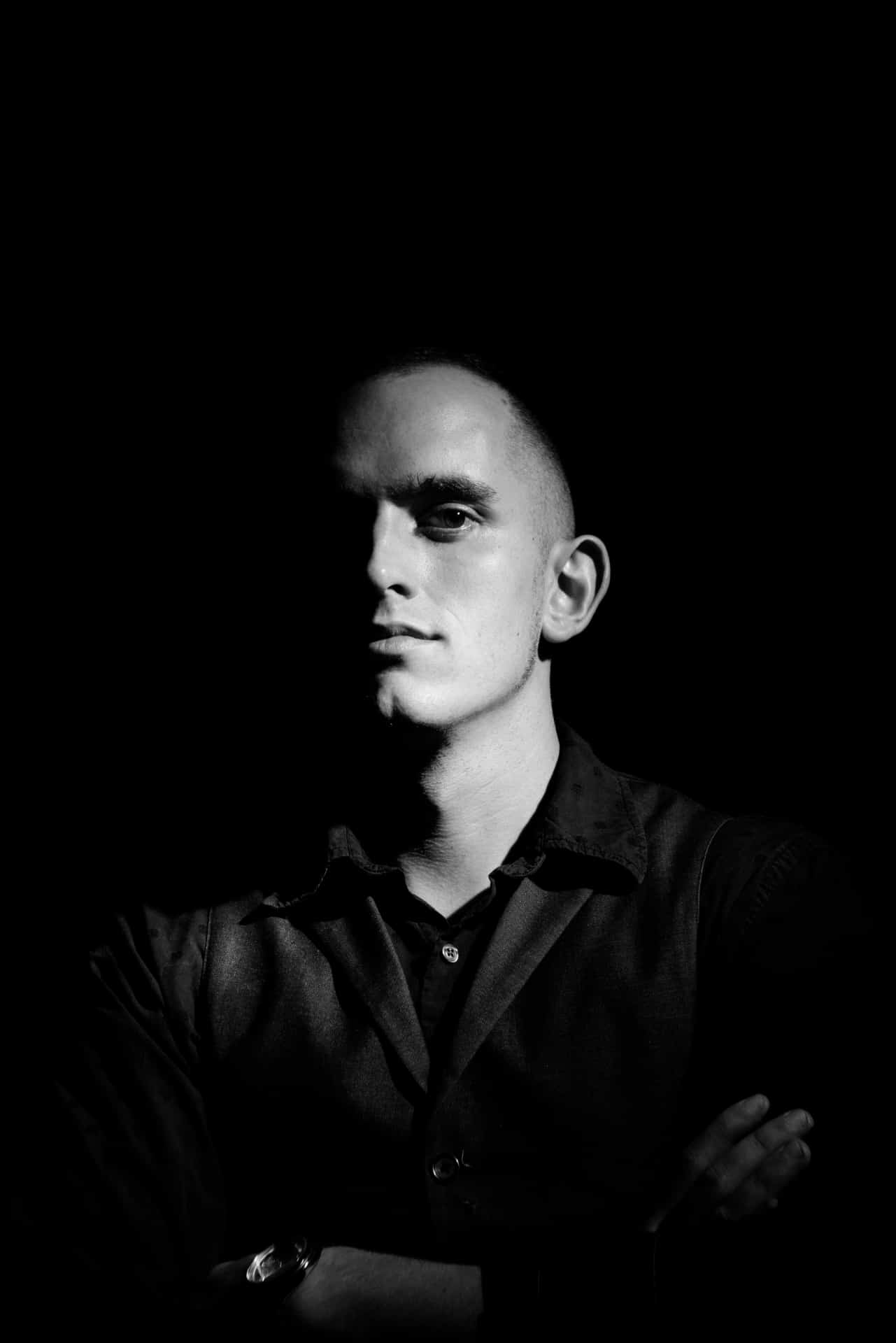 Black and white portrait of a young man with confident expression, cross arms, studio lighting, professional model for fashion, music, or entertainment content.