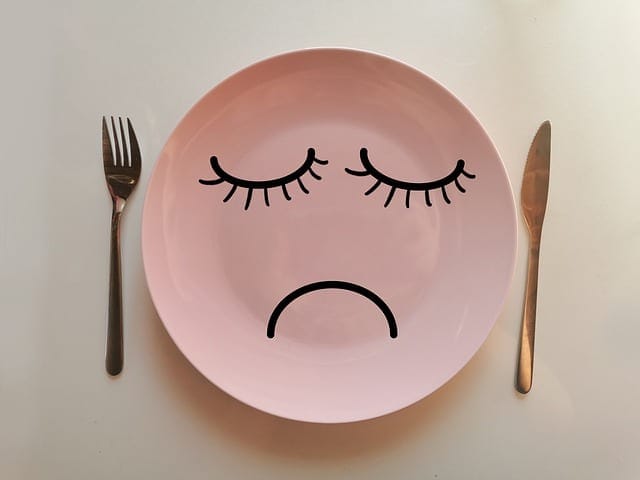Sad face plate with closed eyes and a frown, symbolizing disappointment or sadness, served as a creative prop for food photography or emotional expression in dining scenes.