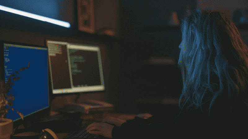 Lines of code on computer screens in a dimly lit tech workspace, symbolizing digital marketing, music industry analytics, or cybersecurity. Suitable for Hypebot articles on music technology, digital marketing trends, or music industry insights.