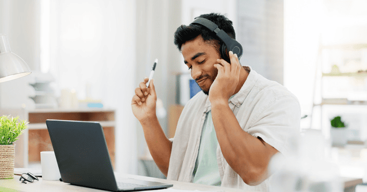 Young man wearing headphones working on a laptop in a bright modern home office environment.