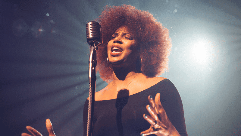 Vocalist performing passionately on stage with professional microphone under bright stage lights, emphasizing music industry and live performance elements.