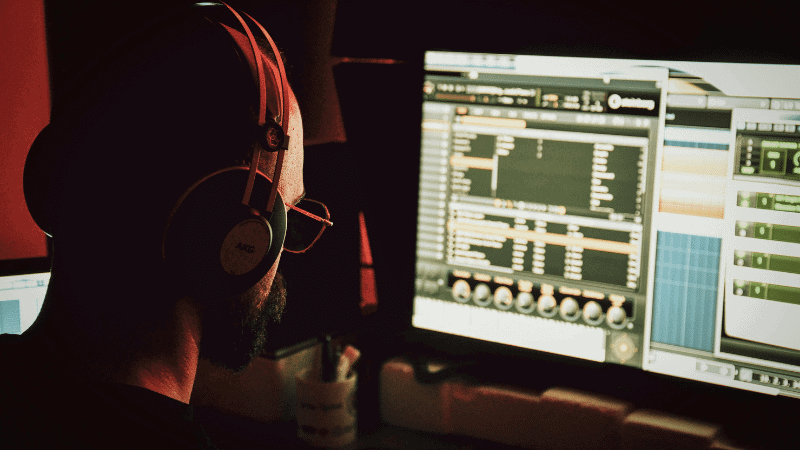 Audio engineer working on music production with digital audio workstation on dual monitors in a dimly lit studio.