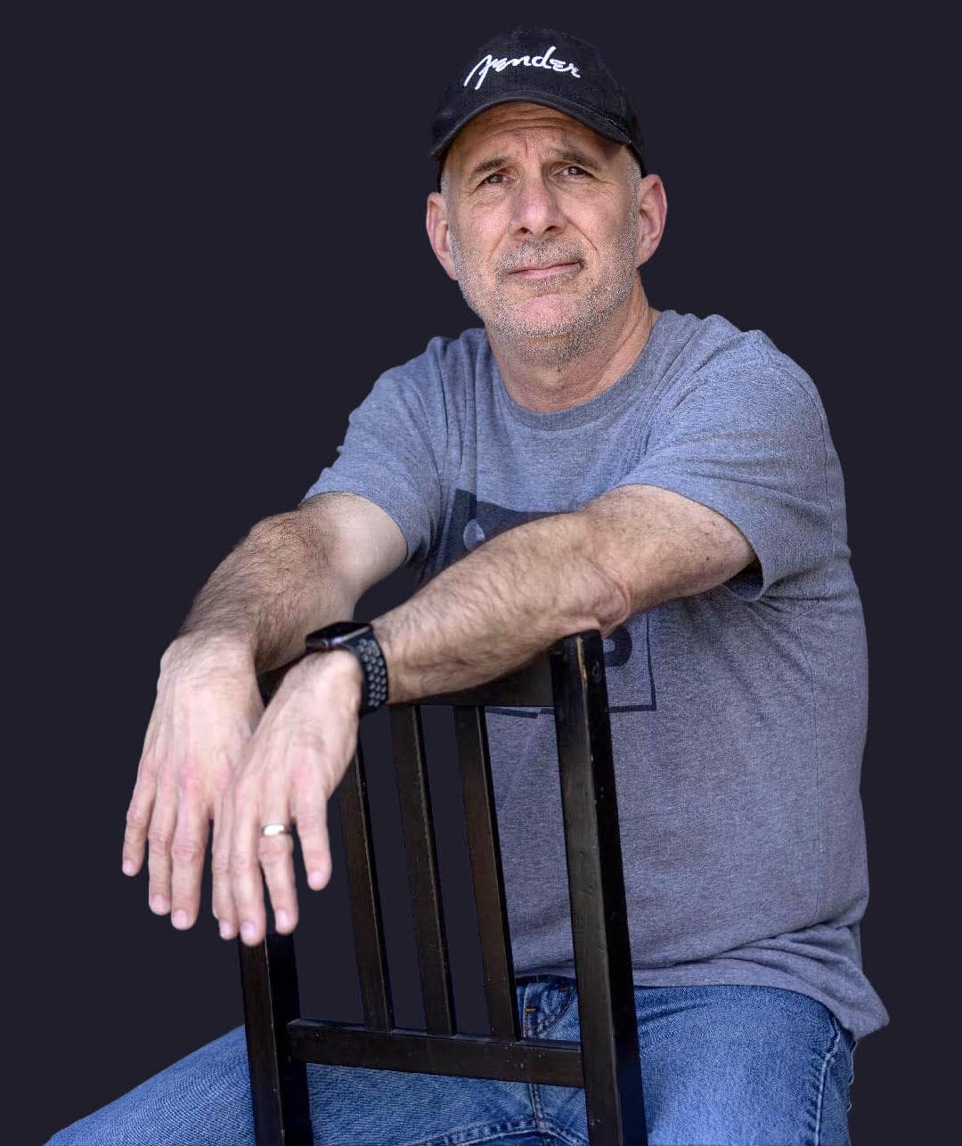 Thoughtful middle-aged man in casual grey t-shirt and black cap sitting on a wooden chair, promoting music industry insights, digital innovation, and creative entrepreneurship for music professionals on Hypebot.