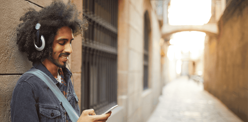 Young man with headphones using a smartphone in an urban alleyway, showcasing music streaming, digital marketing, and social media engagement.