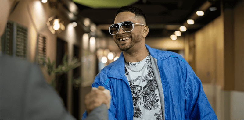 Vibrant man smiling in trendy sunglasses and casual stylish outfit, in a modern indoor setting, representing music industry culture and networking.