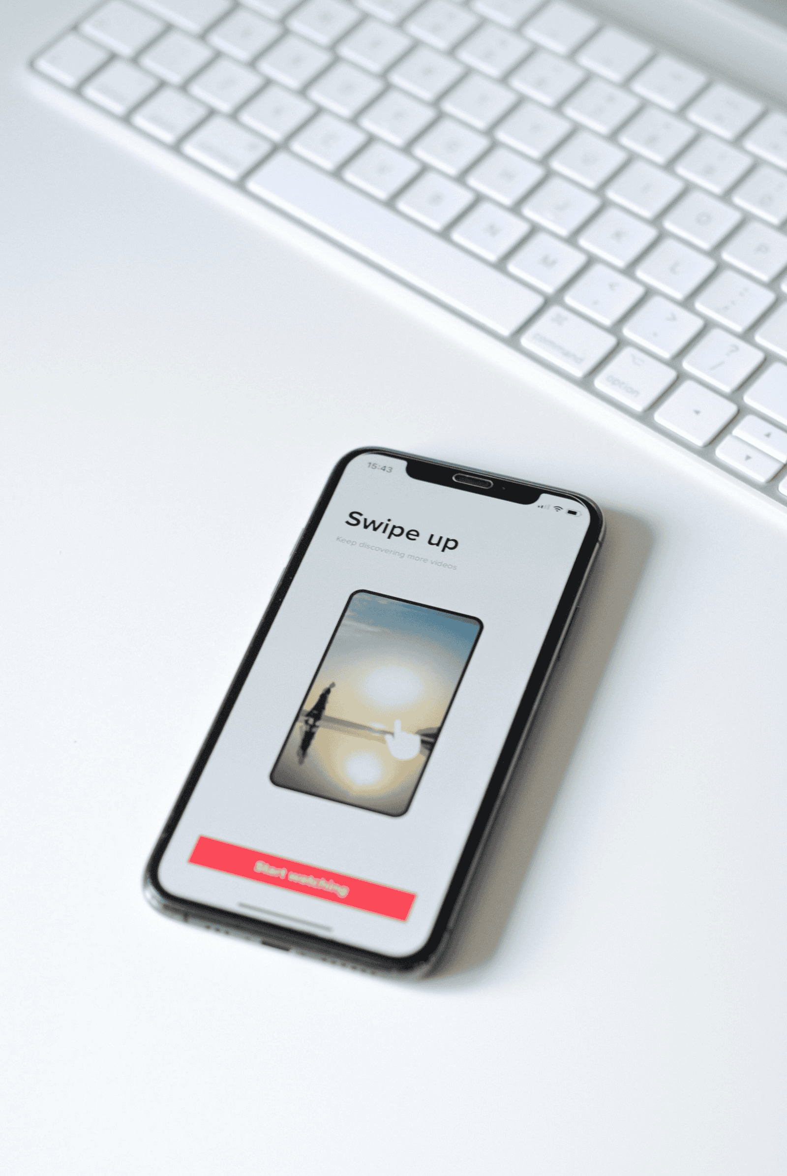 Screenshot of a smartphone displaying a swipe-up video feature on a white desk with a keyboard in the background, illustrating social media content discovery and digital marketing trends.