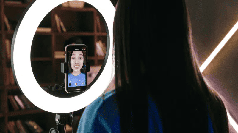 A woman recording a vlog or tutorial using a ring light and smartphone for high-quality video content creation.