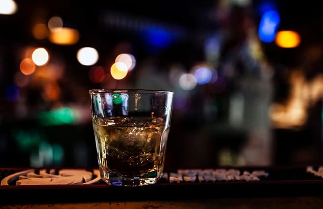 A glass of whiskey on a bar counter with blurred bokeh lights in the background, capturing a nightlife scene.