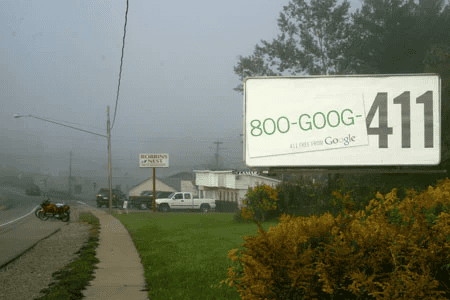 800-GOOG 411 directory assistance billboard on foggy day in small town, featuring Google branded phone number, alongside street and vehicle scene for local search and advertising context.