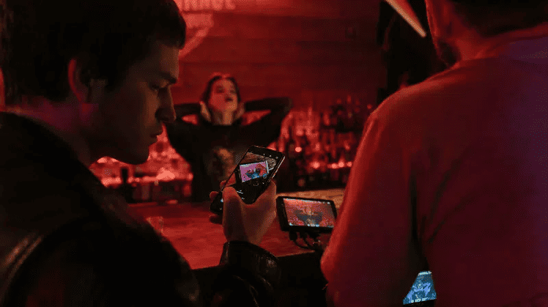 Photo of young people recording a music performance on smartphones at a dimly lit music venue, capturing live entertainment moments for social media sharing.
