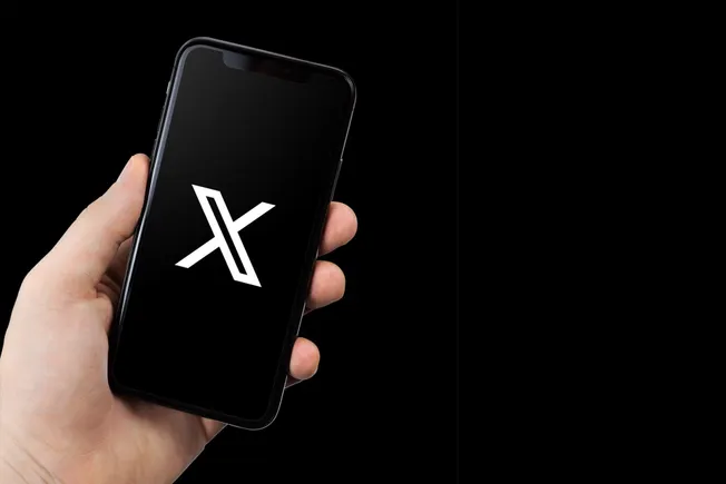 Hand holding a phone showing the X logo