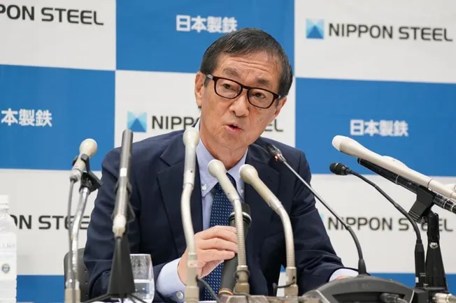 Nippon Steel executive at a press conference in front of company logos