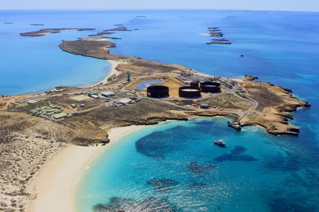 Aerial view of a rocky island in turquoise water with oil storage tanks