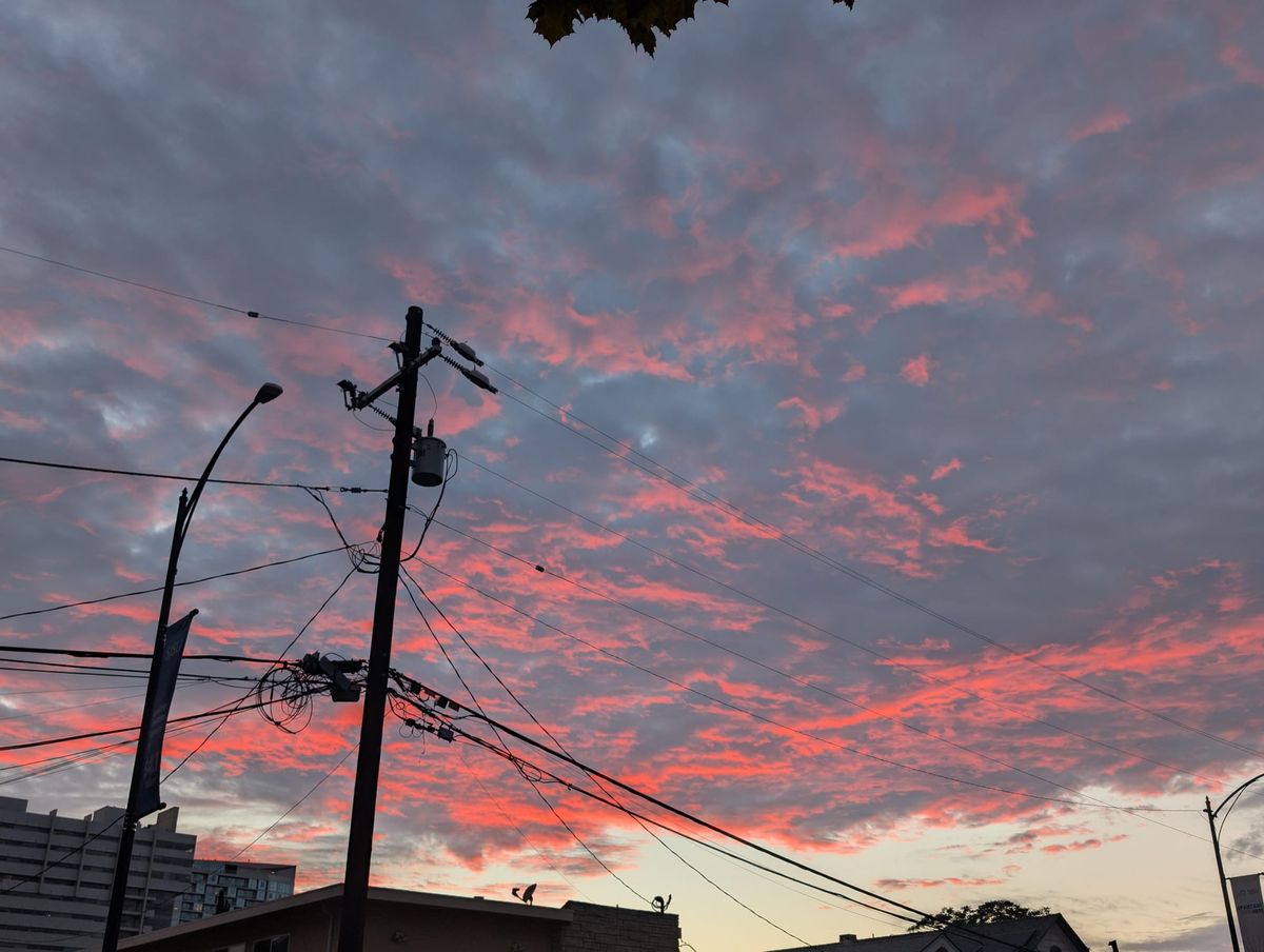 a picture of a sunset with vivid orange, red and grey clouds. From the camera angle, the powerline with wires stretched out of both sides looks tall enough to pierce the clouds
