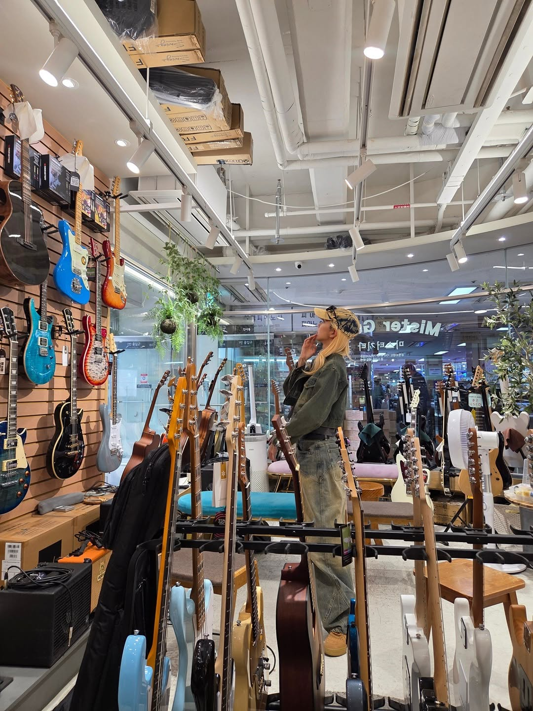 Dami with a thoughtful expression on her face as she looks up at guitars on display in a shop.