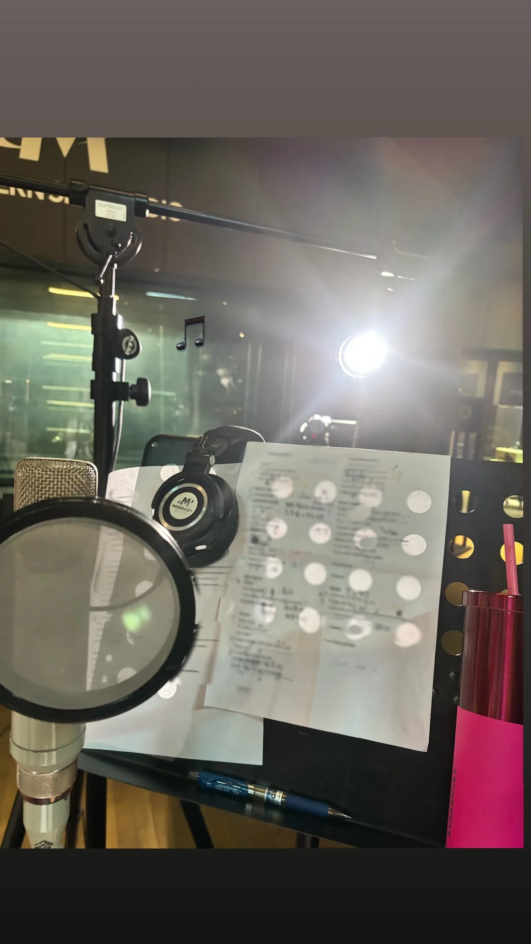 Picture of a recording studio setup from the singer's point of view with microphone/filter and lyrics.