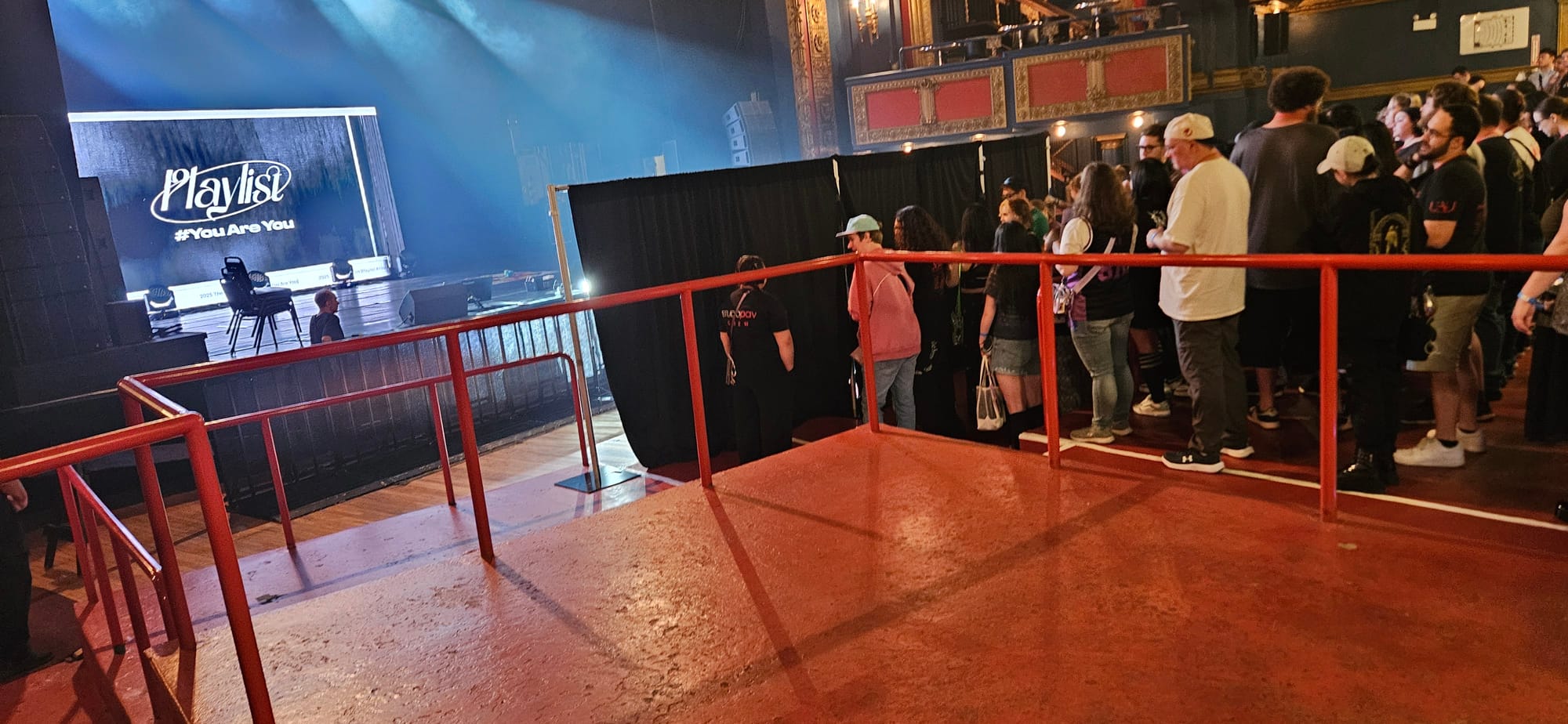 Fans in a crowd lined up to the right with the stage visible with the UAU Playlist logo.