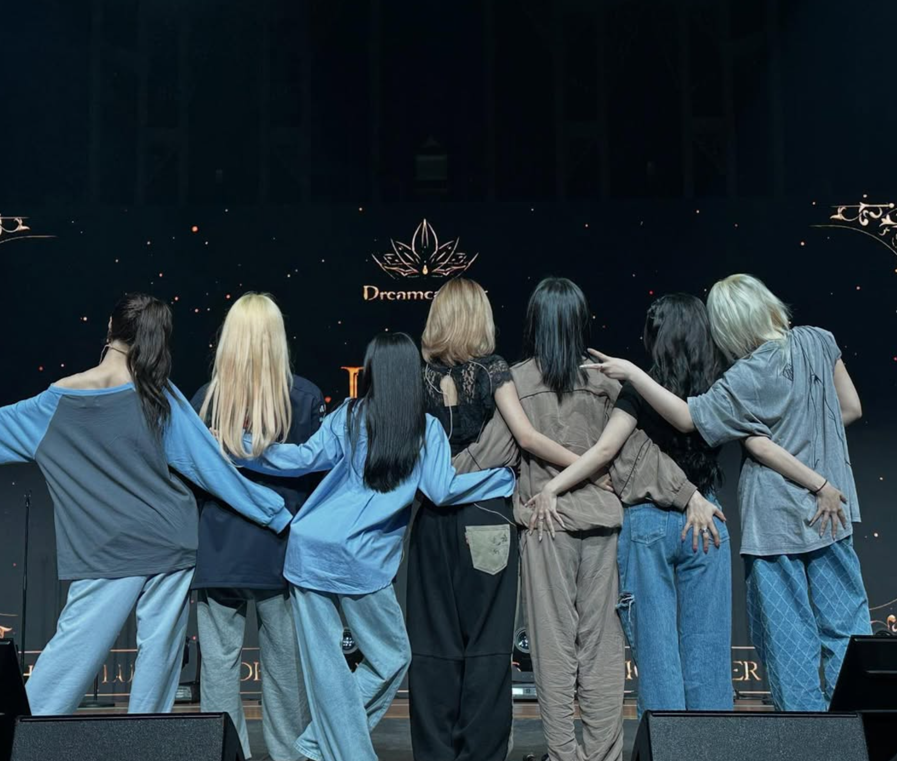 Dreamcatcher posing together during rehearsal with their backs to the camera.