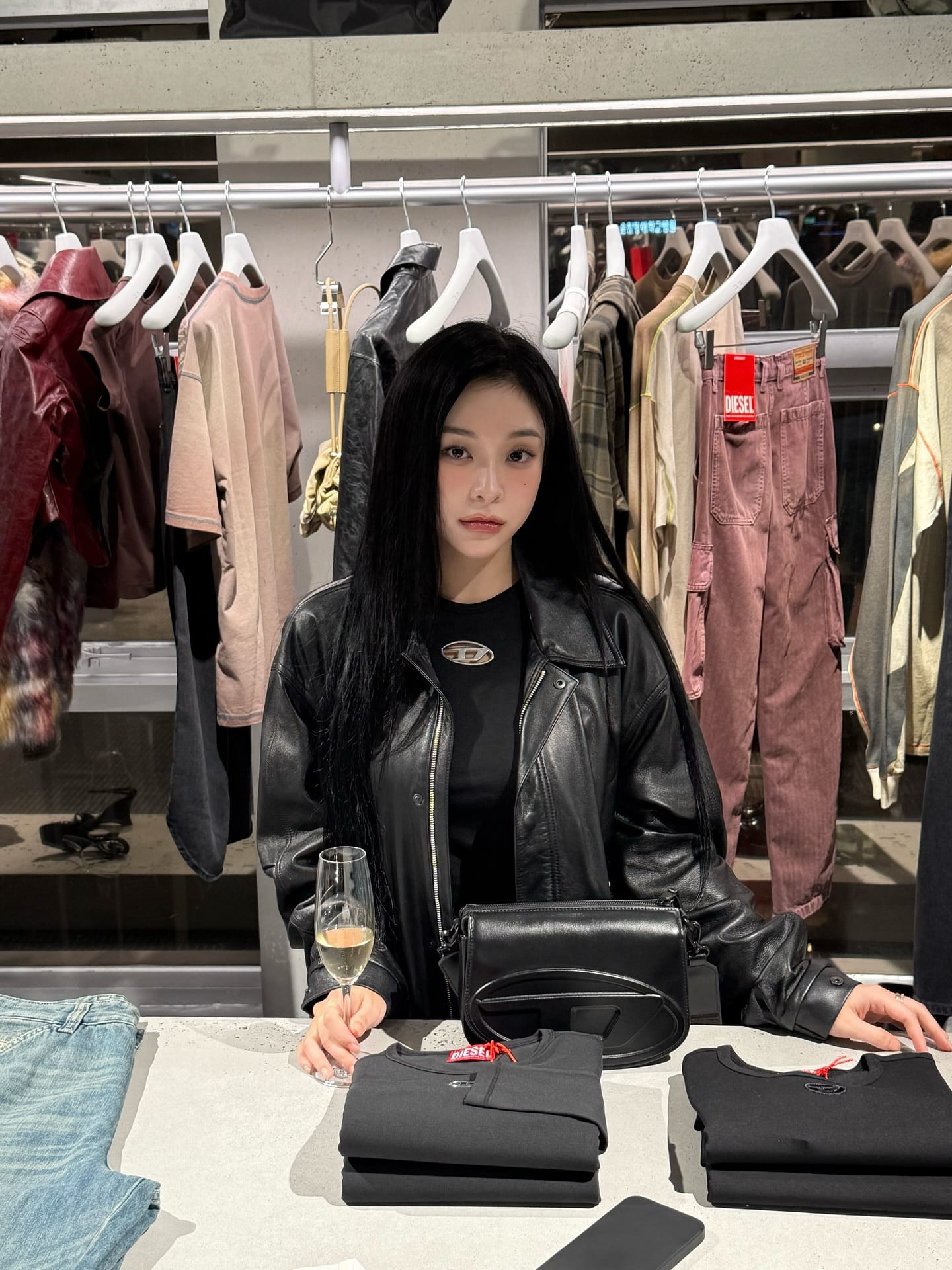 Gahyun holding a wine glass at the Diesel store in Seoul, dressed in black.