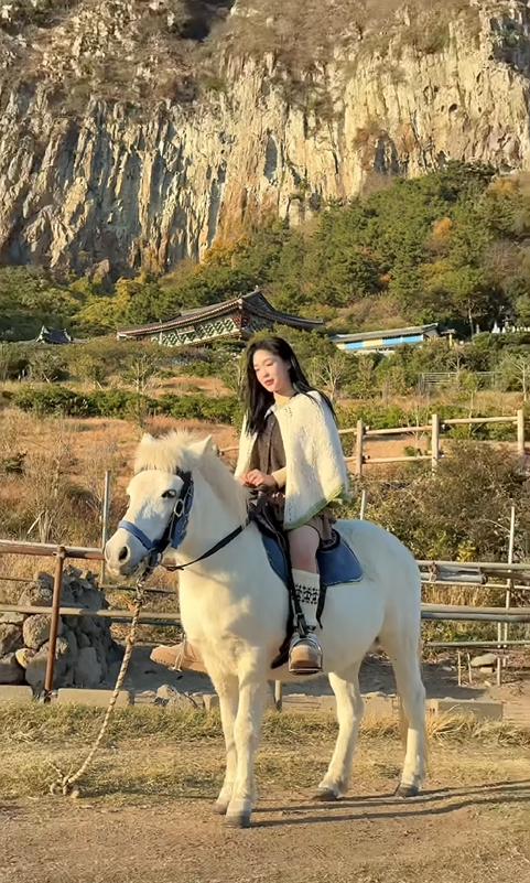 Dreamcatcher Gahyun on a white horse with the Korean countryside in the background.