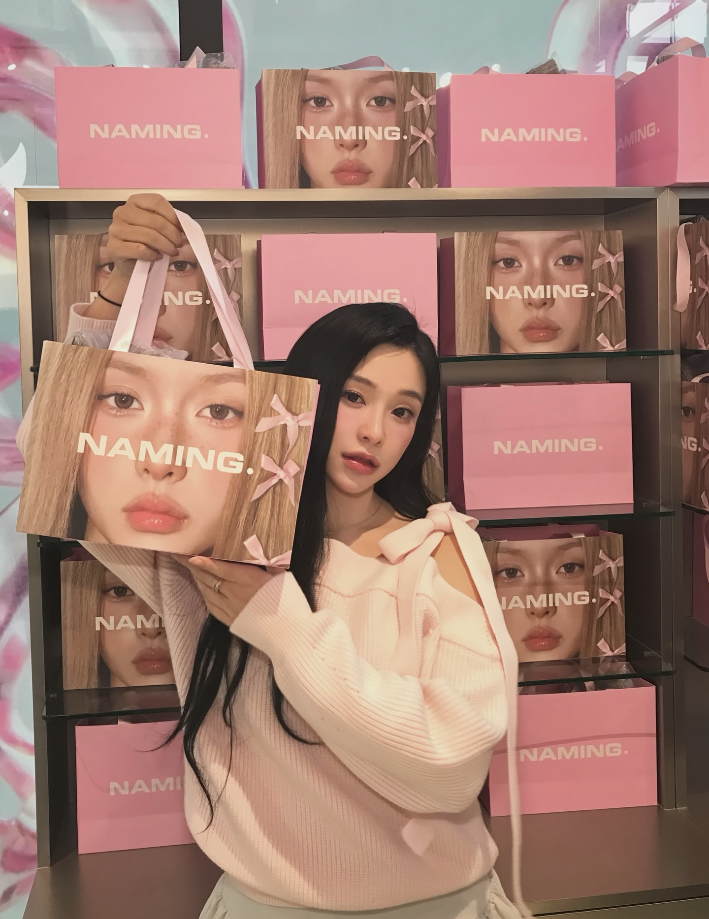 Gahyun in a pink sweater and black hair showing off a naming cosmetic bag.
