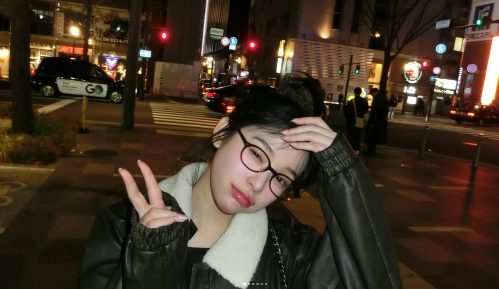 Gahyun, now known as Lee Seoyul, does a victory sign for the camera while smiling and wearing glasses in the city at night.