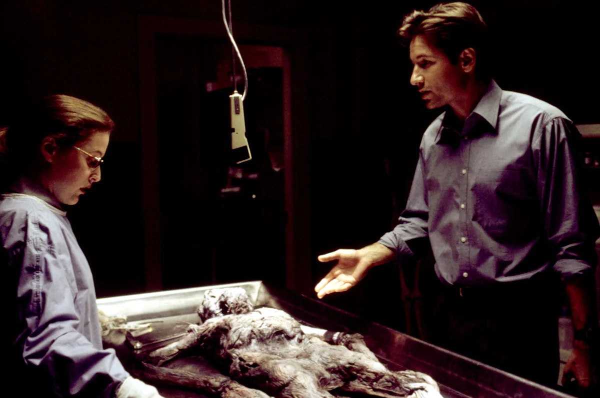 An old body lies on an autopsy table as Mulder and Scully discuss their findings.