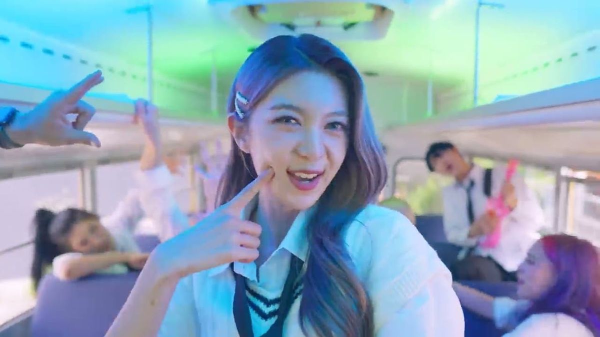 Dreamcatcher's Dami, clad in a school unitform and pants, smiles for the camera on a school bus.