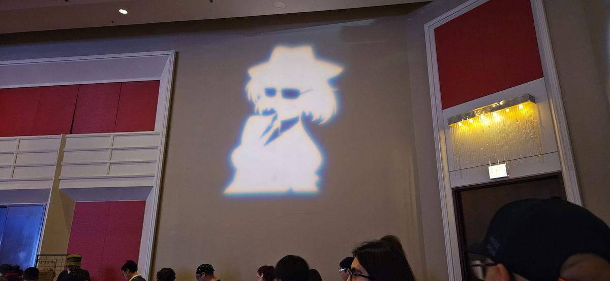 White-colored silhouette of one of the Anime Central logos - a Blues Brothers-style shadow of a girl wearing a hat and sunglasses - is projected onto the main programming hall.
