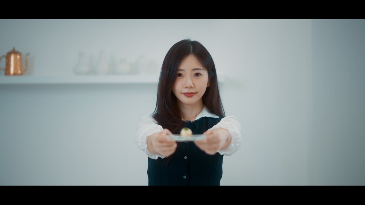 JiU smiling at the camera as she offers a small plate with a cheese spread and garnish.