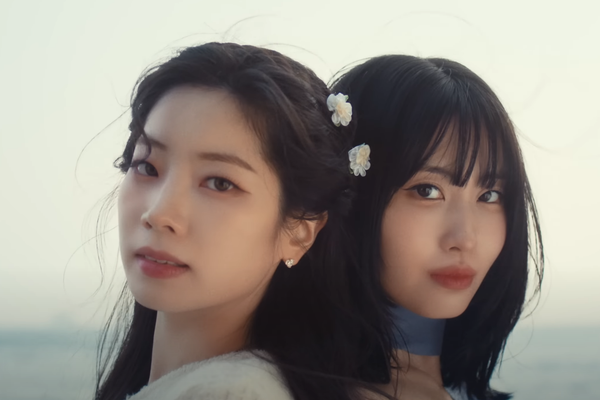 Dahyun and Momo from TWICE look at the camera against a background of the coast