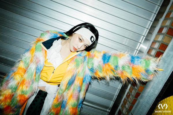 Chung Ha, clad in a rainbow-colored fur and white headband, posing with her arm outstretched.