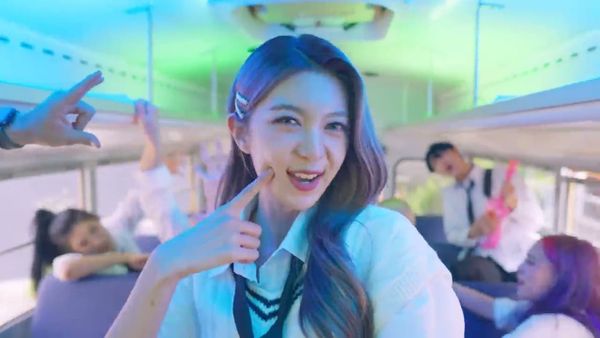 Dreamcatcher's Dami, clad in a school unitform and pants, smiles for the camera on a school bus.