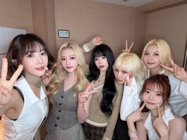 Dreamcatcher poses for the camera in a dressing room with victory signs and smiles.