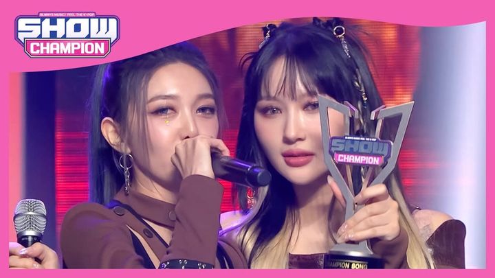 Dami holding the mic up and rapping as Siyeon shows off Dreamcatcher's 1st Music Show Trophy on Show Champion.