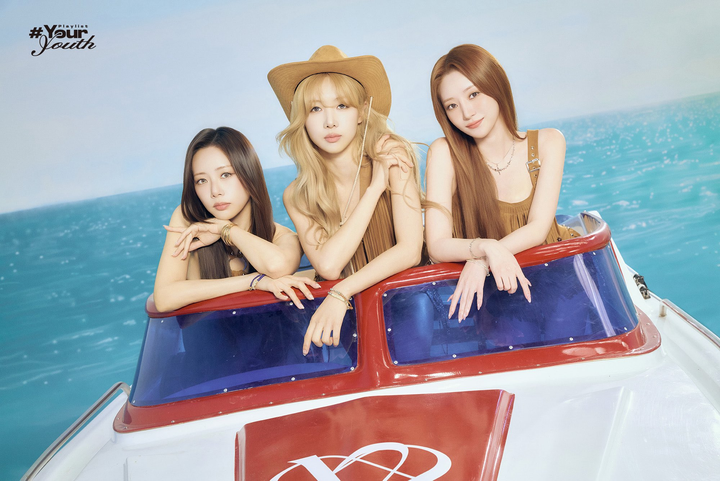 JiU, Yoohyeon (in a cowboy hat) and SuA, standing on a speedboat setpiece in an ocean background.