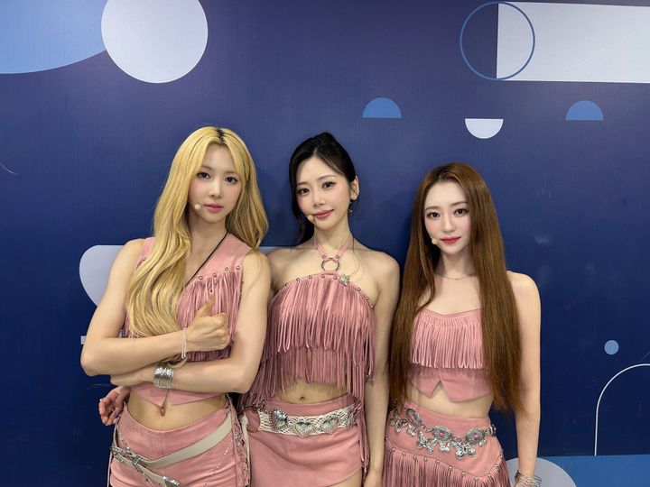 Yoohyeon, JiU, and SuA in pink outfits, smiling for the camera at SBS Inkigayo.