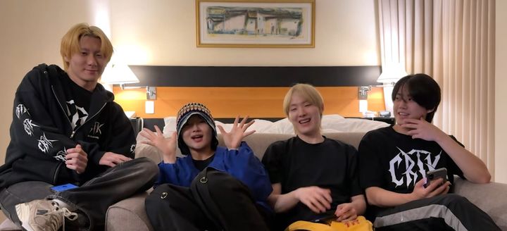 ChRocktikal band members sit on a couch smiling and waving to fans in a YouTube video.