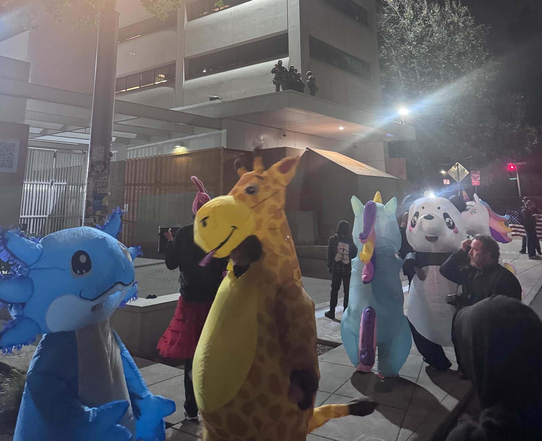 A zoo of creatures is watched by masked goons above.