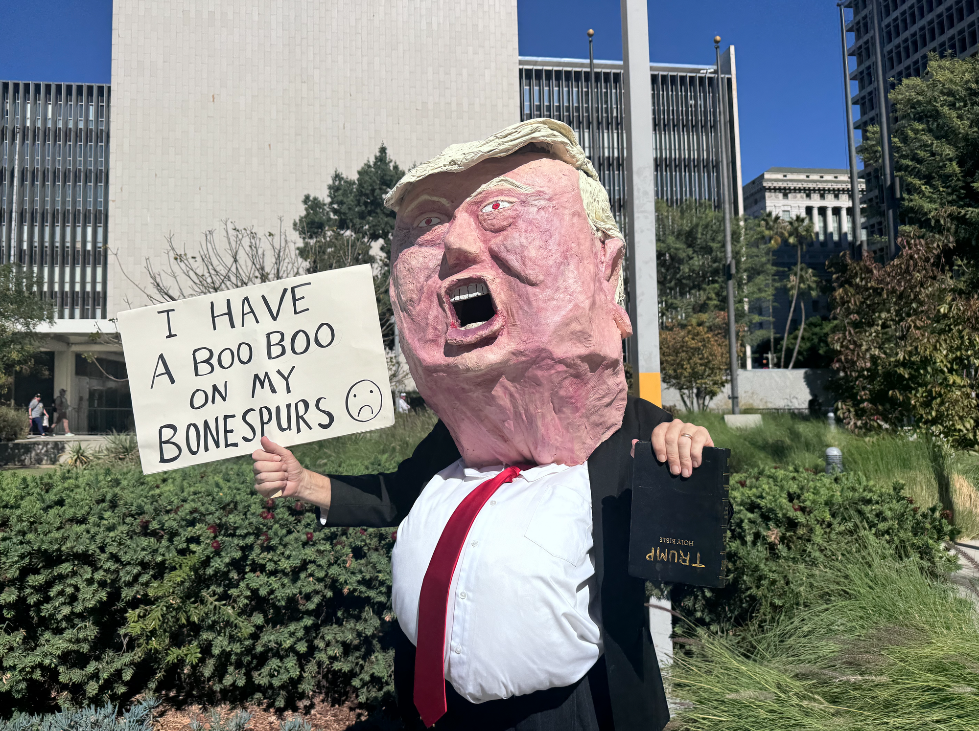 Guy in a Trump head made of paper mache clutching upside down Bible