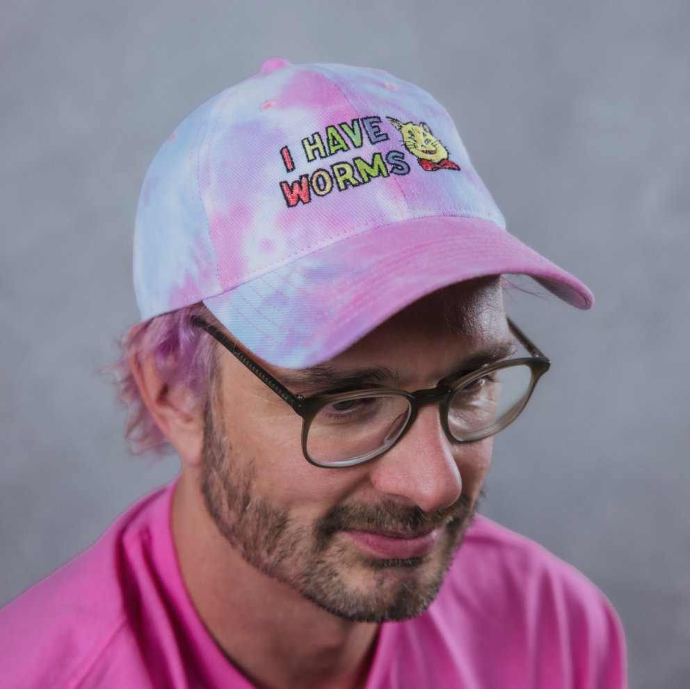 Tie dye rainbow cap with an image of a cat and the words I HAVE WORMS on it